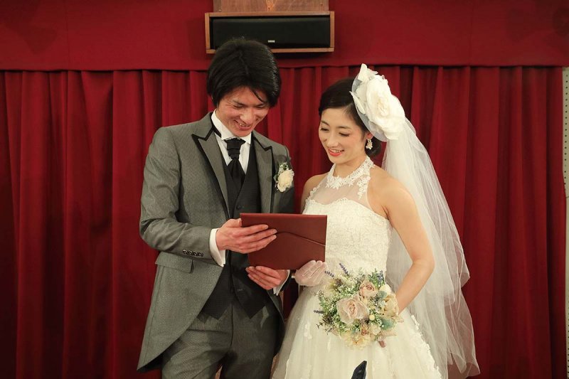ウェディングドレス姿の女性とタキシードを着た男性が誓いの言葉を見ながら微笑んでいる写真