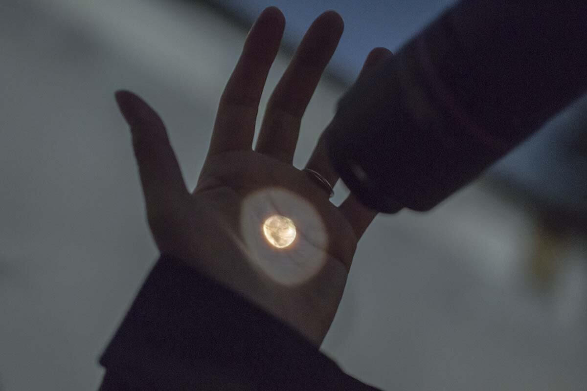 天体望遠鏡を使って手のひらに月を映している写真